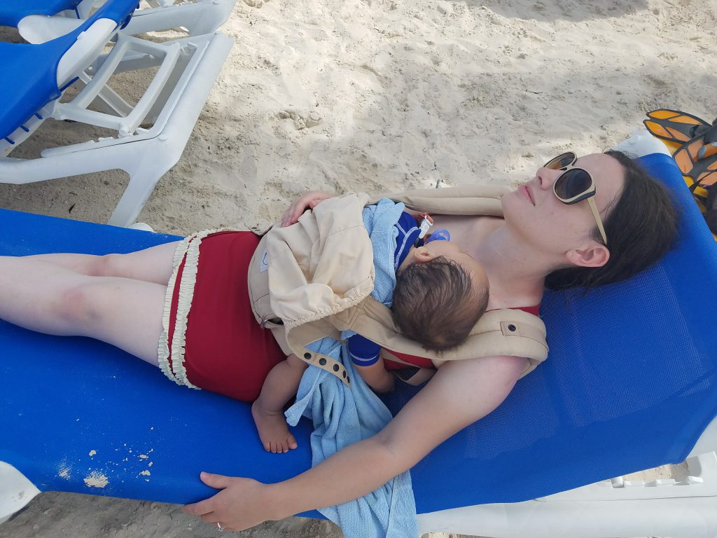 Mom wearing a sleeping baby in a baby carrier on the beach