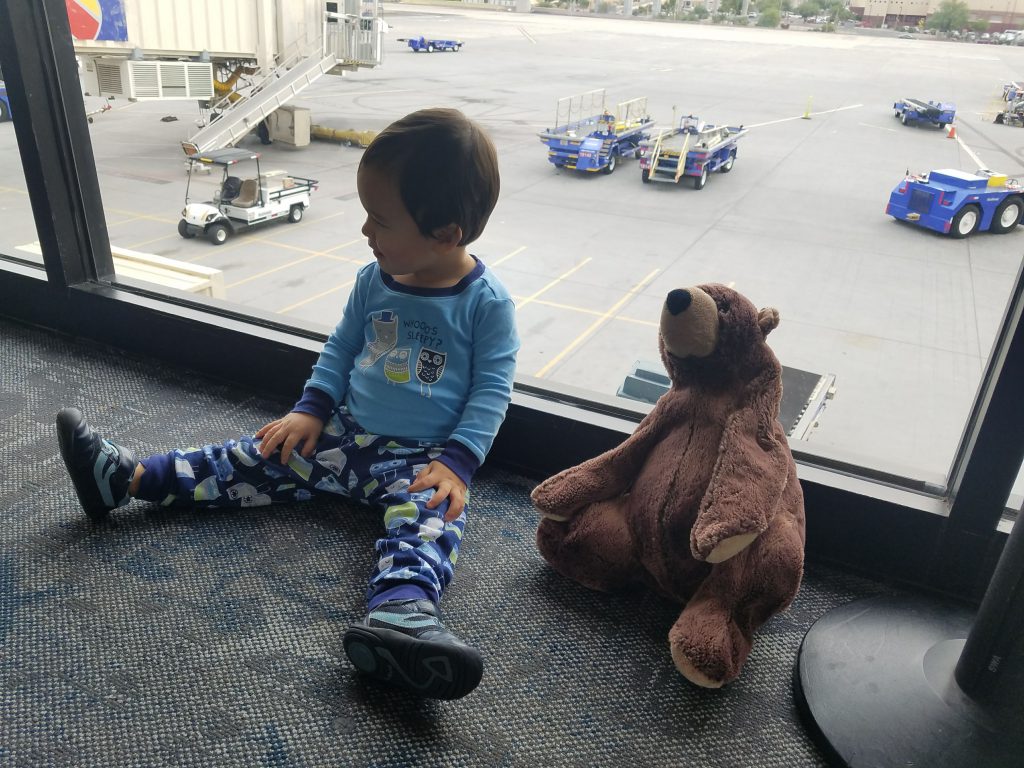 Toddler and his stuffed bear sitting by an airport window