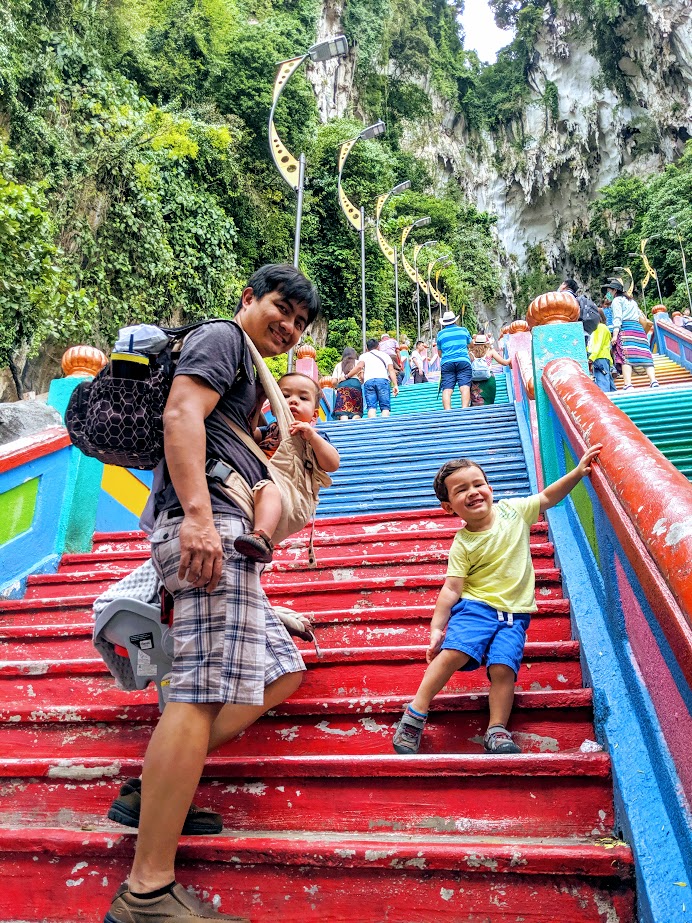 A man with a baby in a baby carrier and a little boy standing on colorful steps