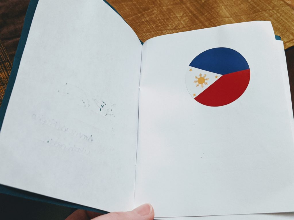 Putting a flag sticker in a paper passport for a Philippines preschool unit