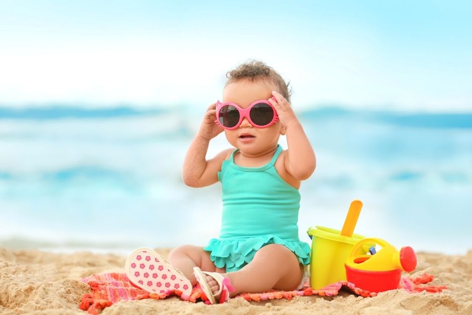 Toddler on the beach wearing sunglasses- beach essentials for toddlers and babies