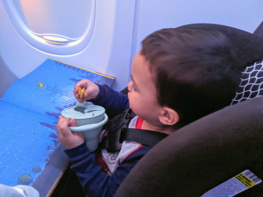 Toddler entertained on a plane eating a snack from a snack catcher