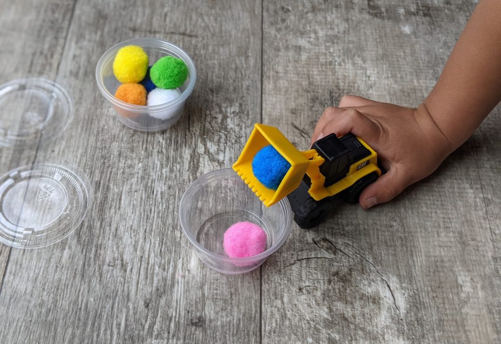 Child putting pom poms into containers with small truck