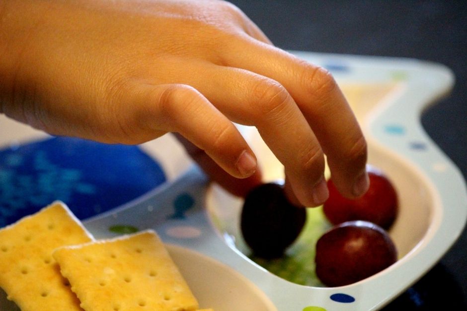Child picking up grapes from a tray of grapes and crackers