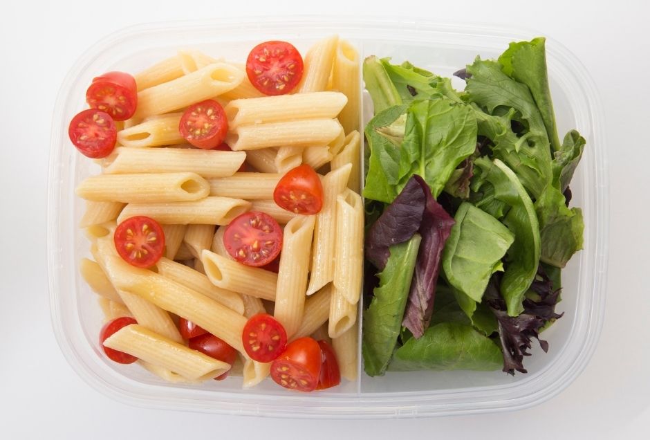 A container packed with pasta salad and green salad