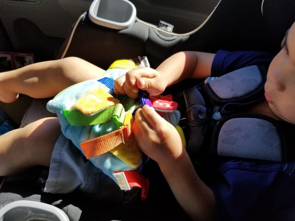 Child playing with a buckle toy in the car- toddler road trip activities