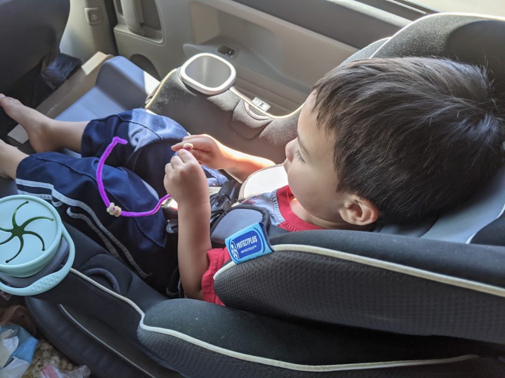 Child putting Cheerios on a pipe cleaner- toddler road trip activities