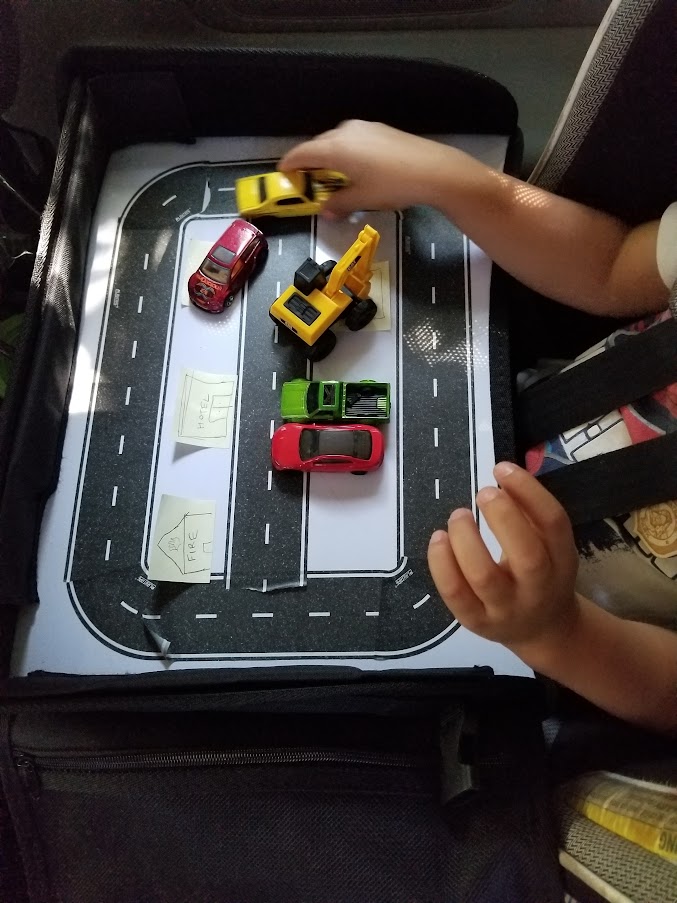 Child playing with cars on a tape road attached to a lap tray in the car