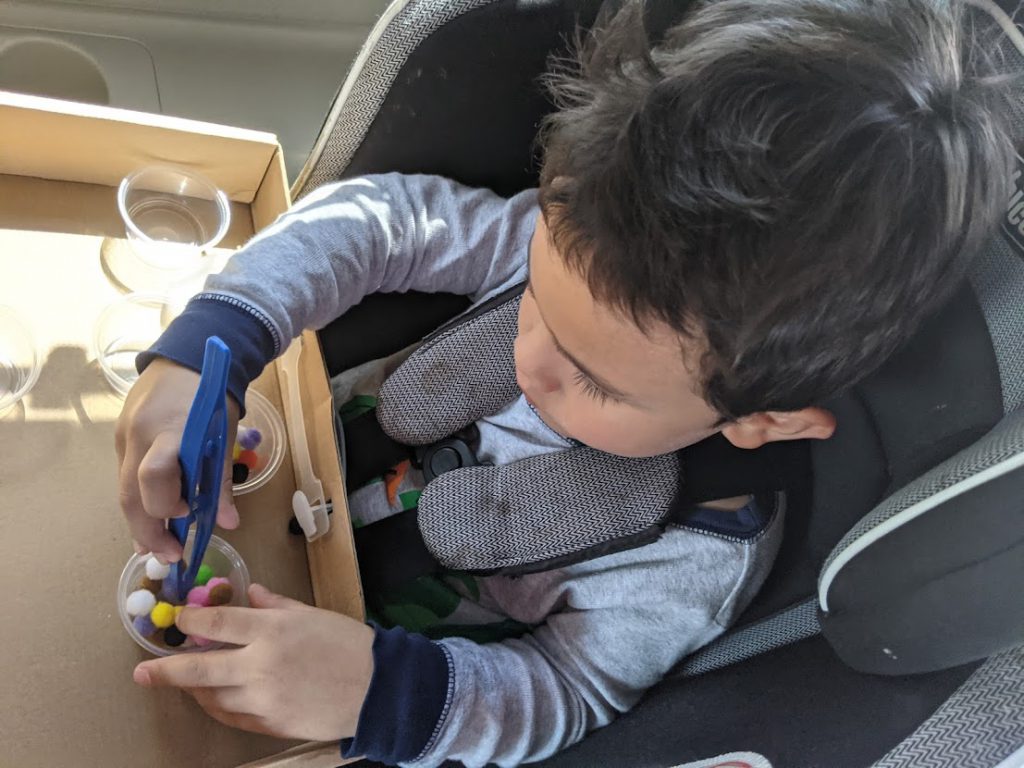 Child using tweezers to move pom poms from one container to another