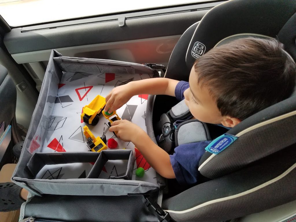 Child playing with miniature trucks in the car- toddler road trip activities