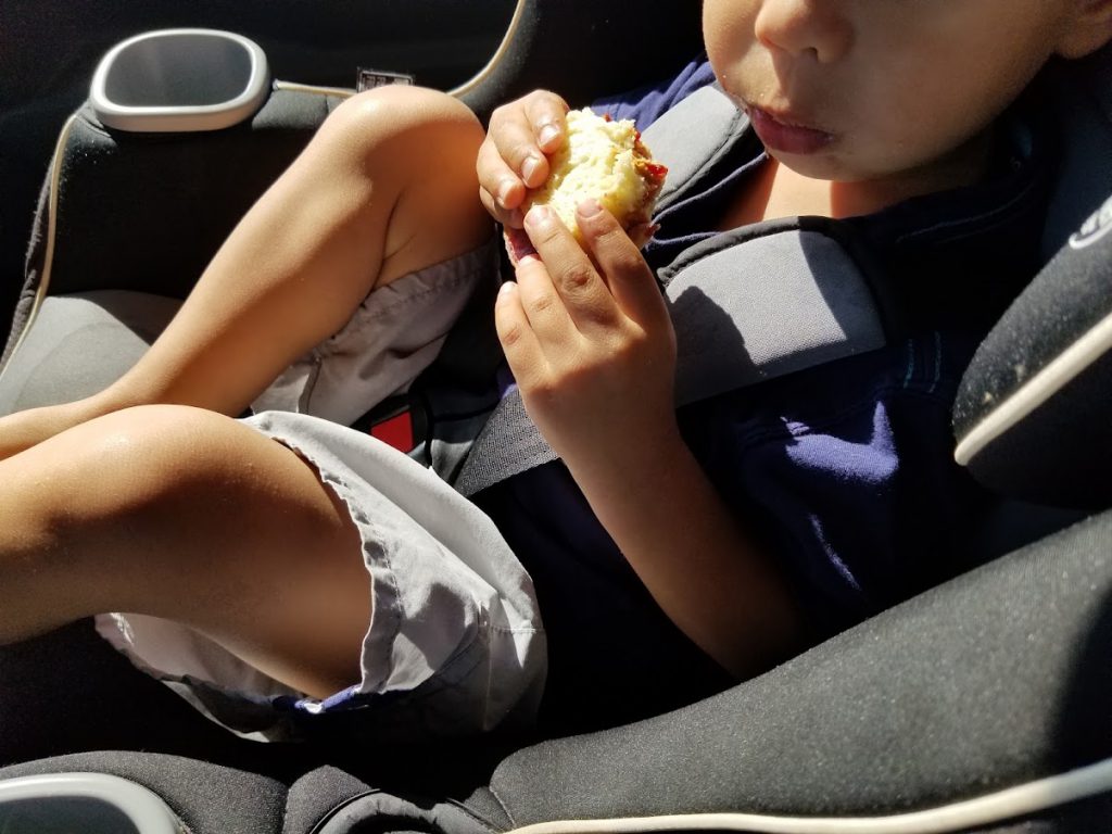 Toddler eating a peanut butter and jelly sandwich on a road trip
