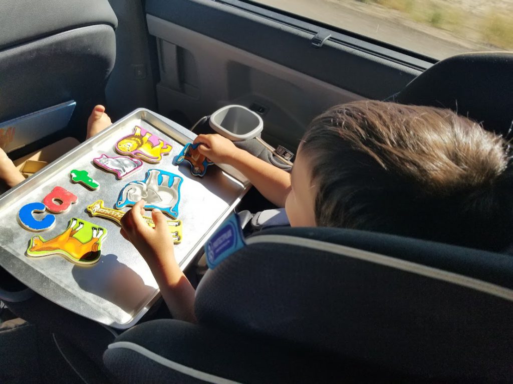 Child putting magnets of letters and animals on a cookie sheet- toddler road trip activities