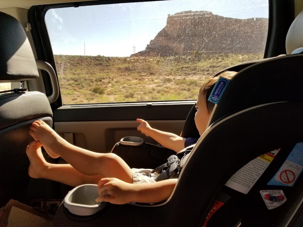 Child in a car seat looking out the window in the car- toddler road trip activities