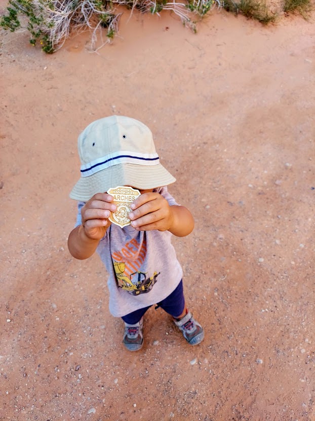 Child holding a Junior Park Ranger badge- Arches National Park with Kids