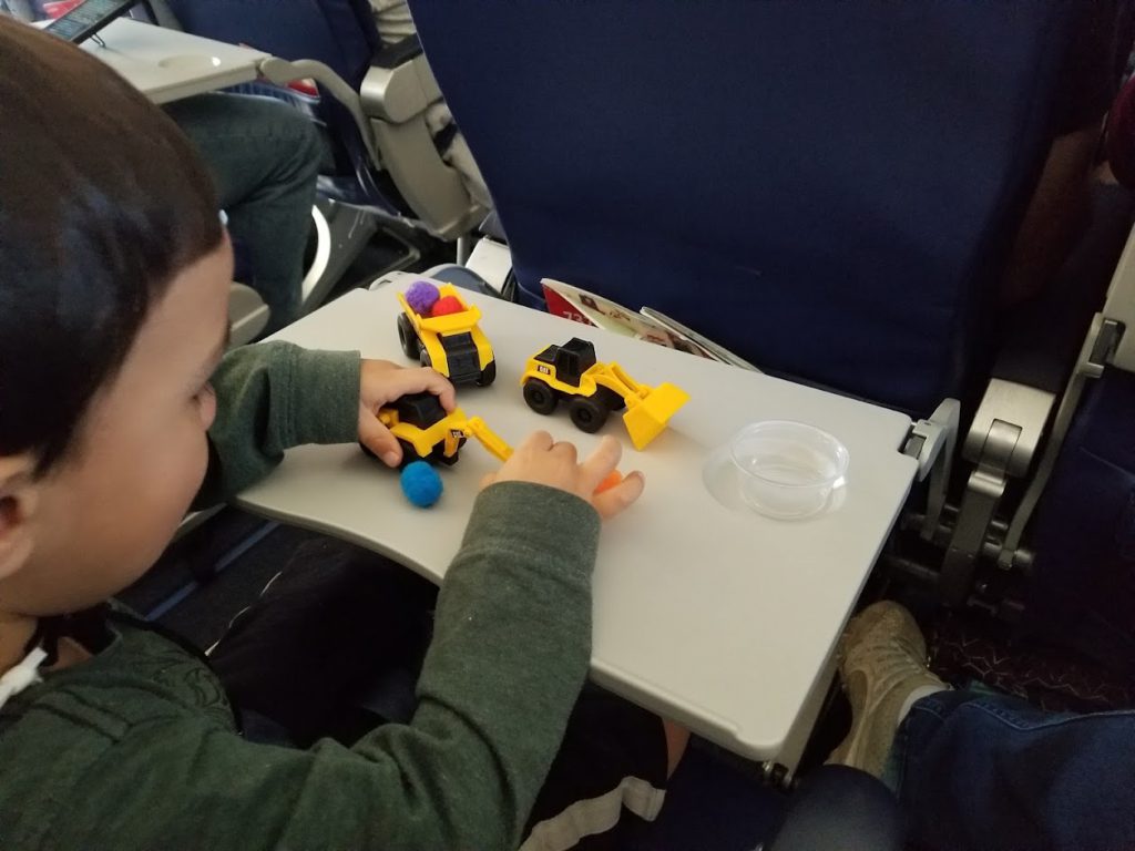 Child on a plane playing with miniature trucks- toddler airplane activities