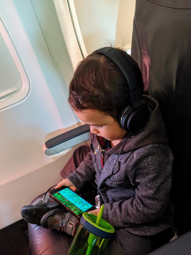 Child on a plane wearing headphones and watching a show on a phone