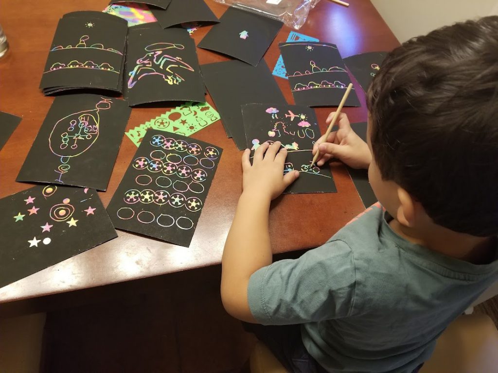 Child working on a scratch art set at a table in a hotel