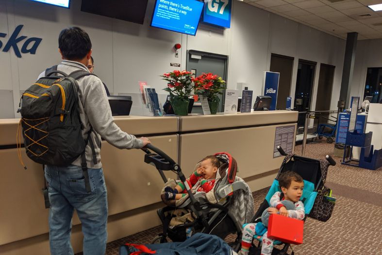 Man talking to a gate agent at the airport with two kids in strollers