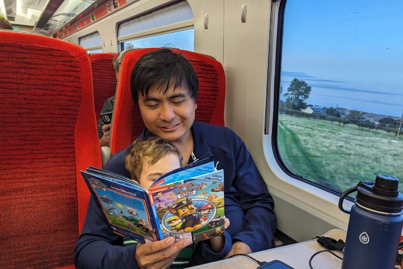 Father reading a book to a toddler on a train