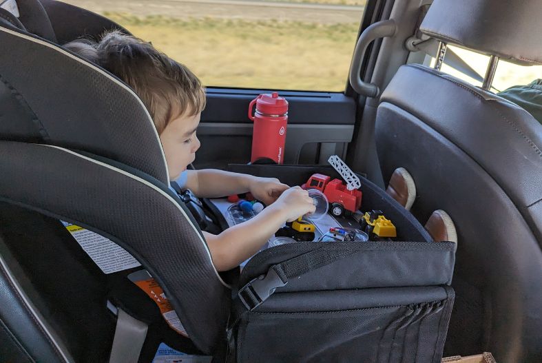 Child in the car playing with trucks and road tape on a travel tray