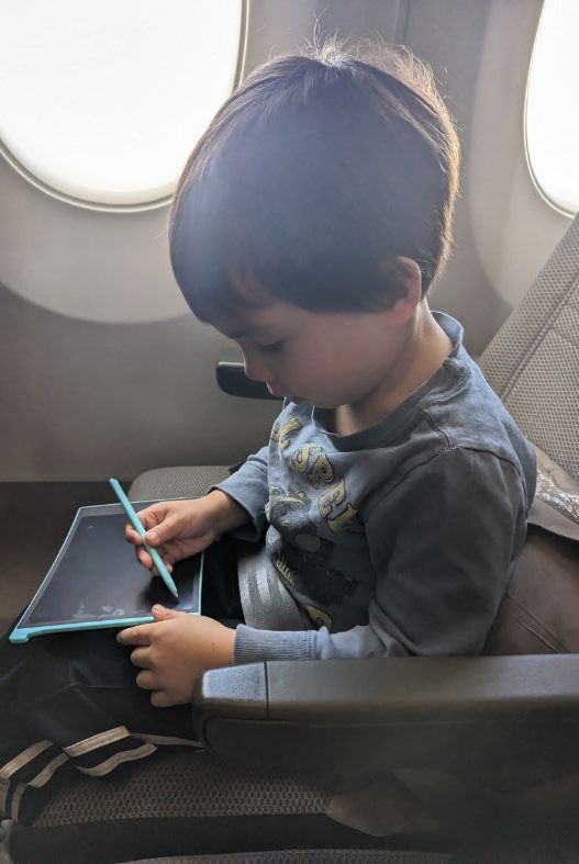 Child using a drawing tablet on the plane-best travel toys for 3 year olds