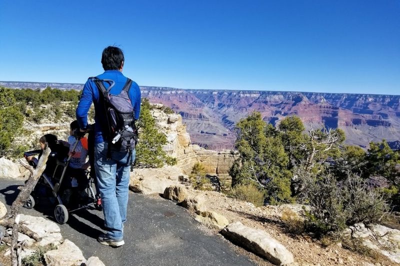 Man walking along the rim of the Grand Canyon pushing a stroller